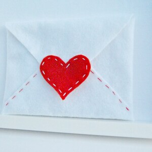 May include: A white envelope with a red felt heart sewn on the front. The heart has white stitching around the edges.