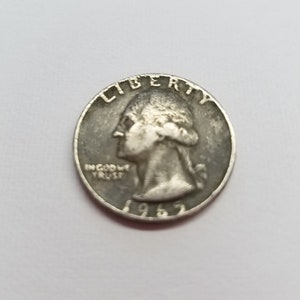 May include: A silver US quarter dollar coin with the year 1965 and the words "Liberty" and "In God We Trust" on the front.