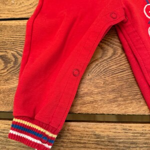 Puede incluir: Mono rojo para beb&eacute; con pu&ntilde;o a rayas de colores. El mono tiene cierres de presi&oacute;n y un gr&aacute;fico de globos. El pu&ntilde;o presenta rayas blancas, azules, amarillas y rojas.