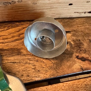 May include: A silver metal cookie cutter shaped like a rose with a round center hole. The cutter is on a wooden surface.
