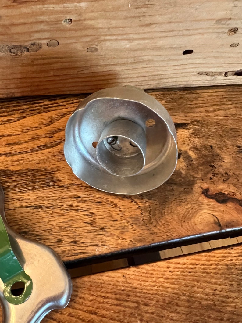 May include: A silver metal cookie cutter shaped like a rose with a round center hole. The cutter is on a wooden surface.