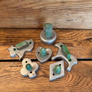 May include: A set of six vintage metal cookie cutters with green wooden handles. The cutters are shaped like a heart, a diamond, a clover, a horse, a bunny, and a round cutter.
