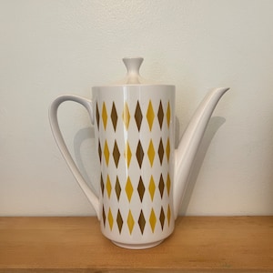 May include: White ceramic teapot with a brown and yellow diamond pattern. The teapot has a lid and a spout.