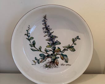 May include: A white ceramic bowl with a gold rim features a botanical illustration of a purple flower with green leaves and the text "Ajuga reptans".