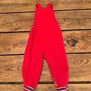 Puede incluir: Mono rojo para beb&eacute; con tirantes. Los pu&ntilde;os y los lados del mono tienen un estampado a rayas en azul, amarillo y blanco. El mono est&aacute; hecho de un material suave.