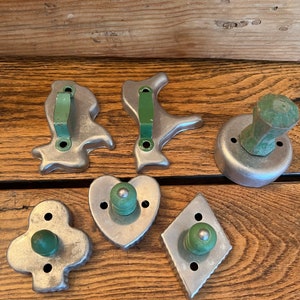 May include: Six vintage metal cookie cutters with green wooden handles. The cutters are shaped like a heart, a diamond, a clover, a bird, a dog, and a round cutter.