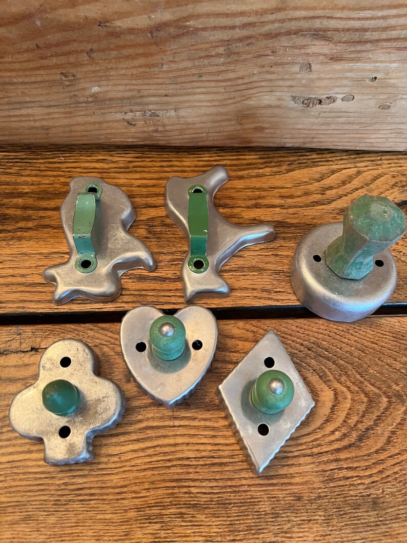 May include: Six vintage metal cookie cutters with green wooden handles. The cutters are shaped like a heart, a diamond, a clover, a bird, a dog, and a round cutter.