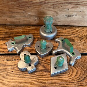 May include: A set of six vintage metal cookie cutters with green wooden handles. The cutters are shaped like a heart, a diamond, a club, a dog, a cat, and a round cutter.