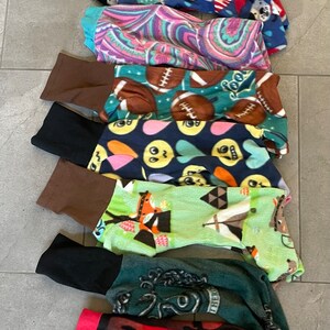 May include: A collection of pet pajamas in various patterns. Designs include stars, flags, paisley, footballs, smiley faces, and a zombie theme. Each pajama has a contrasting cuff at the ankle.