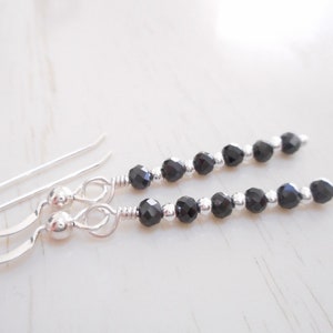 May include: A pair of silver dangle earrings with black faceted beads. The earrings have a simple hook fastening.