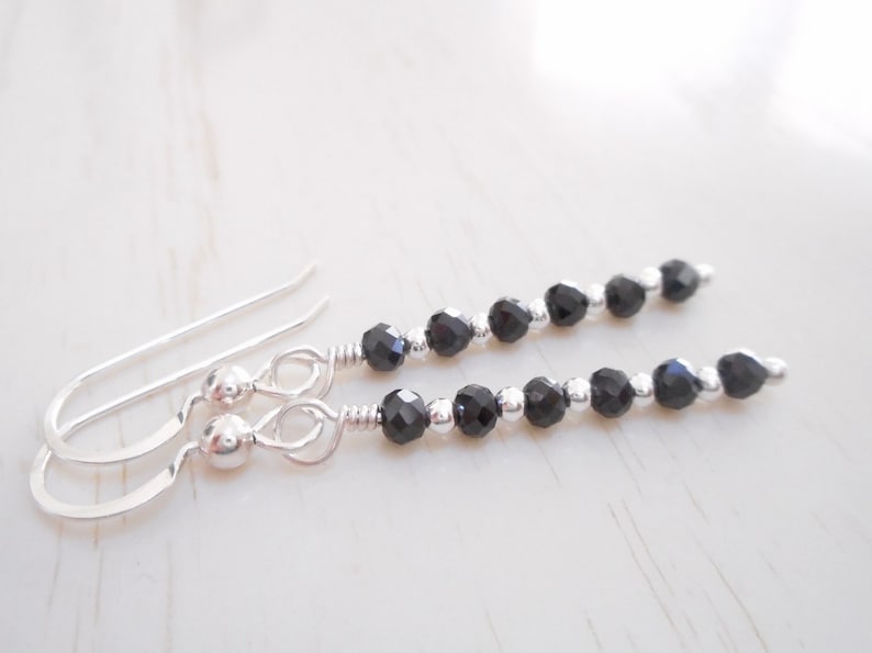 May include: A pair of silver dangle earrings with black faceted beads. The earrings have a simple hook fastening.