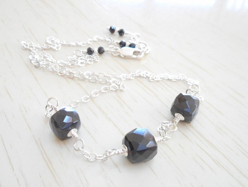 May include: A silver chain necklace with three black faceted gemstone beads.