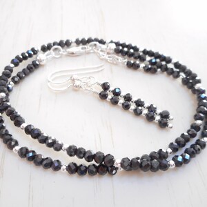 May include: A black spinel necklace and earrings set with silver accents. The necklace is a double strand of faceted black spinel beads.