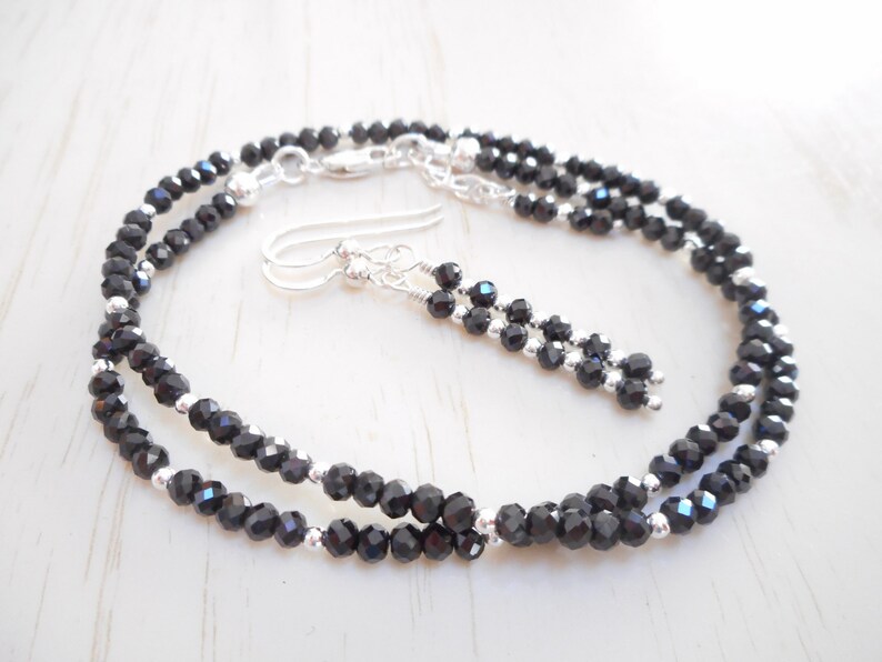 May include: A black spinel necklace and earrings set with silver accents. The necklace is a double strand of faceted black spinel beads.