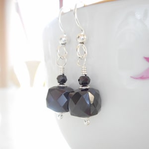 May include: A pair of silver dangle earrings with black faceted gemstone drops.
