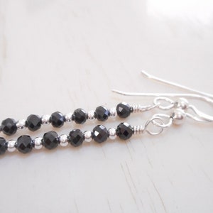 May include: A pair of silver dangle earrings featuring black faceted beads. The earrings have a simple design and are ideal for everyday wear.