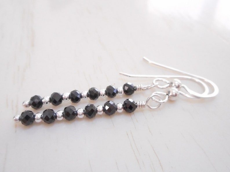 May include: A pair of silver dangle earrings featuring black faceted beads. The earrings have a simple design and are ideal for everyday wear.