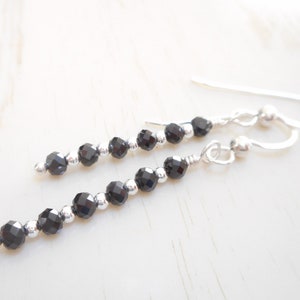 May include: A pair of silver dangle earrings with black faceted beads. The earrings are approximately 5 cm long.