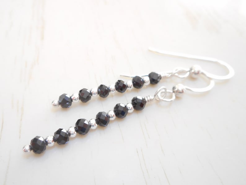 May include: A pair of silver dangle earrings with black faceted beads. The earrings are approximately 5 cm long.