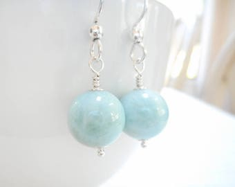May include: A pair of silver earrings with light blue round gemstone beads.