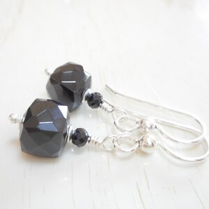 May include: A pair of silver dangle earrings with black faceted gemstone beads. The earrings have a simple design and are perfect for everyday wear.