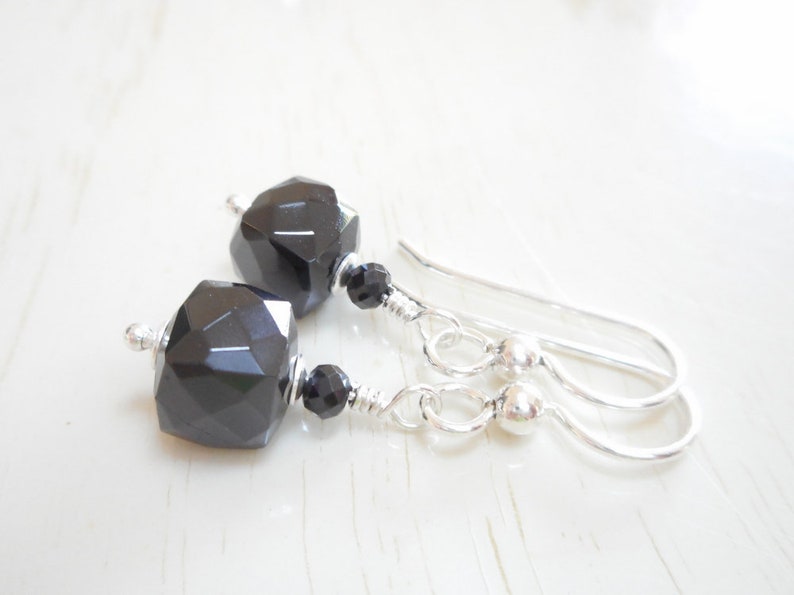 May include: A pair of silver dangle earrings with black faceted gemstone beads. The earrings have a simple design and are perfect for everyday wear.