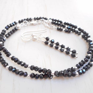 May include: A black spinel necklace and earrings set with silver accents. The necklace is a double strand of faceted black spinel beads.