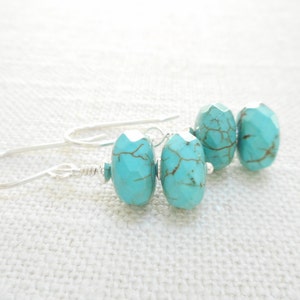 Puede incluir: Pendientes colgantes de turquesa con ganchos de plata. Las piedras turquesa son de color azul claro con vetas marrones.