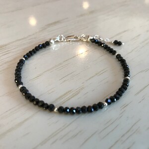 May include: A black beaded bracelet with silver accents. The bracelet is made of small, round beads and has a simple, elegant design.
