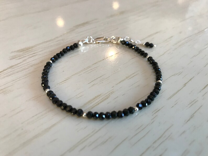 May include: A black beaded bracelet with silver accents. The bracelet is made of small, round beads and has a simple, elegant design.