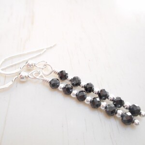 May include: A pair of silver dangle earrings featuring black gemstone beads. The earrings have a simple design and are ideal for everyday wear.