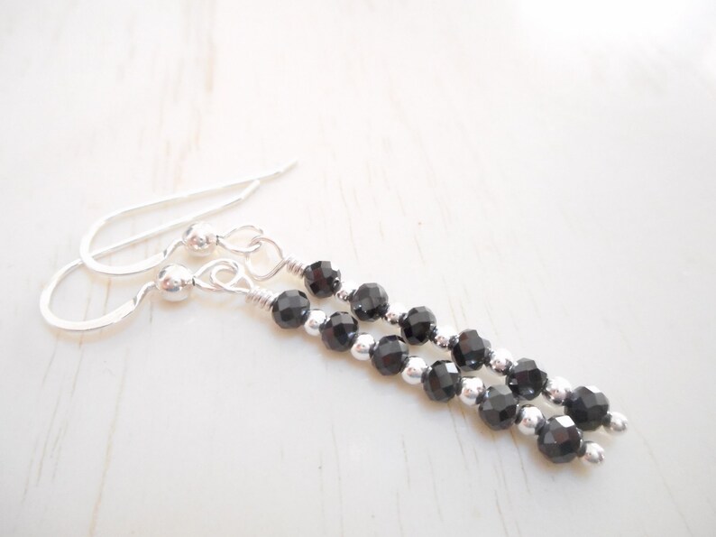 May include: A pair of silver dangle earrings featuring black gemstone beads. The earrings have a simple design and are ideal for everyday wear.