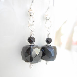 May include: A pair of silver dangle earrings with black faceted gemstone drops. The earrings have a simple design and are perfect for everyday wear.