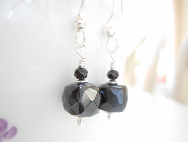 May include: A pair of silver dangle earrings with black faceted gemstone drops. The earrings have a simple design and are perfect for everyday wear.