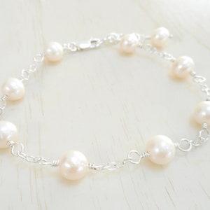 May include: A delicate pearl bracelet with a silver chain. The bracelet features a series of white pearls, each connected by a silver chain link.