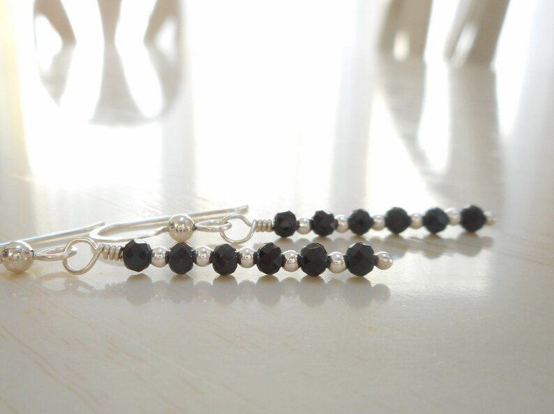 May include: A pair of silver earrings with black beads. The earrings are made with small silver beads and black faceted beads.
