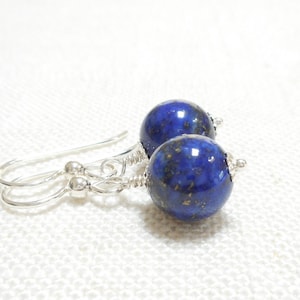 May include: A pair of silver dangle earrings with blue lapis lazuli gemstone beads. The beads have a speckled, glittery appearance.