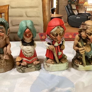 Può includere: Quattro figurine in ceramica fantasiose di personaggi anziani. Le figure includono un uomo in tuta, una donna in abito rosso e altre due figure con tratti del viso unici. Ogni figura è su una piccola base.