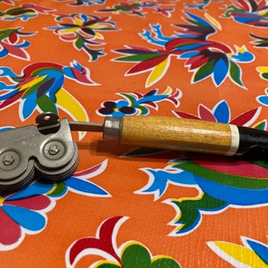 May include: A vintage can opener with a wooden handle and a silver metal cutting mechanism. The opener has two wheels with serrated edges for opening cans.