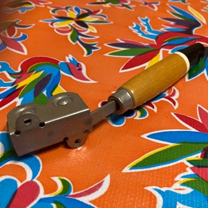May include: A vintage metal and wood can opener with a black and white handle. The opener has a silver metal body with a black handle and a white stripe.