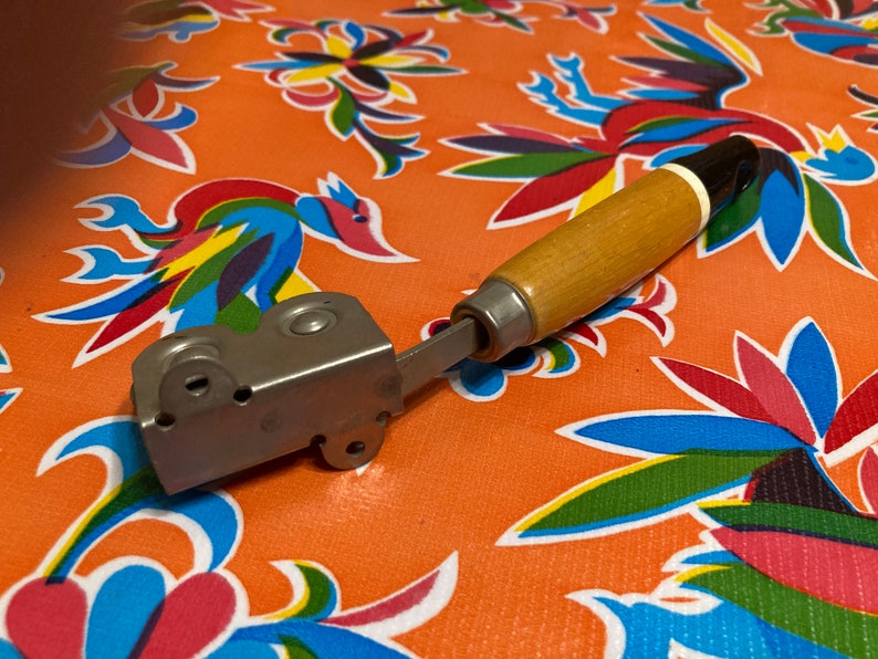 May include: A vintage metal and wood can opener with a black and white handle. The opener has a silver metal body with a black handle and a white stripe.