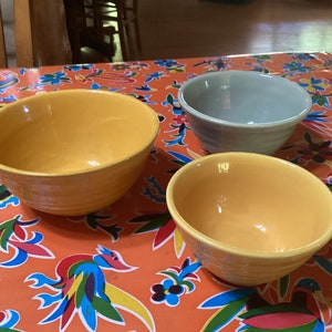 Puede incluir: Tres cuencos de cerámica sobre un mantel colorido. Dos de los cuencos son amarillos y uno es gris claro.