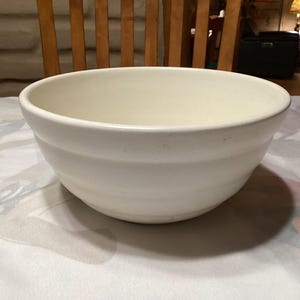 May include: A large, white ceramic mixing bowl with a smooth, rounded interior and a slightly flared rim.