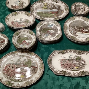 Könnte beinhalten: Eine Sammlung von Vintage-Keramik-Geschirr mit Landschaftsdesigns in Braun, Weiß und Grün. Das Set umfasst Teller, Schalen und eine Tasse, alle mit einer detaillierten, rustikalen Ästhetik. Die Teller variieren in Größe und Form.