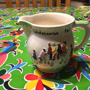 May include: White ceramic pitcher with a colorful illustration of people in a parade. The pitcher has the words "Widecombe Fair" written on it.