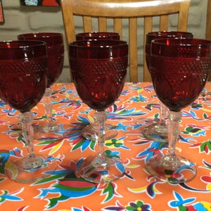 Pode incluir: Seis copos de vinho tinto com um padrão de diamante sobre uma toalha de mesa colorida. Os copos são transparentes e têm uma base com haste.