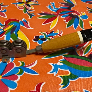 May include: A vintage kitchen tool with a wooden handle and a metal blade with multiple wheels. The handle is brown with a black and white stripe. The tool is on a colorful floral fabric.