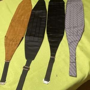 May include: Four cummerbunds in various colors and patterns. One is tan, one is black, one is a darker black, and the last is gray with a geometric pattern. Each has an adjustable strap and metal hardware.