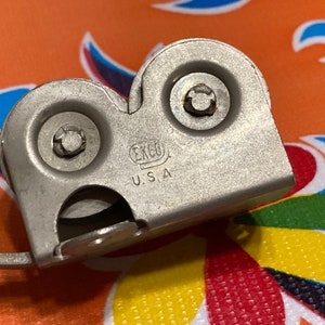 May include: A silver knife sharpener with two sharpening wheels and a handle. The sharpener has the text "ERGO U.S.A." printed on it.