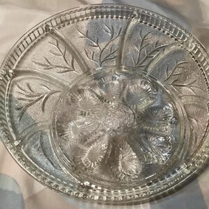 Peut inclure: Un plat de service en verre transparent avec un motif décoratif de feuilles et de fleurs. Le plat est divisé en six sections.